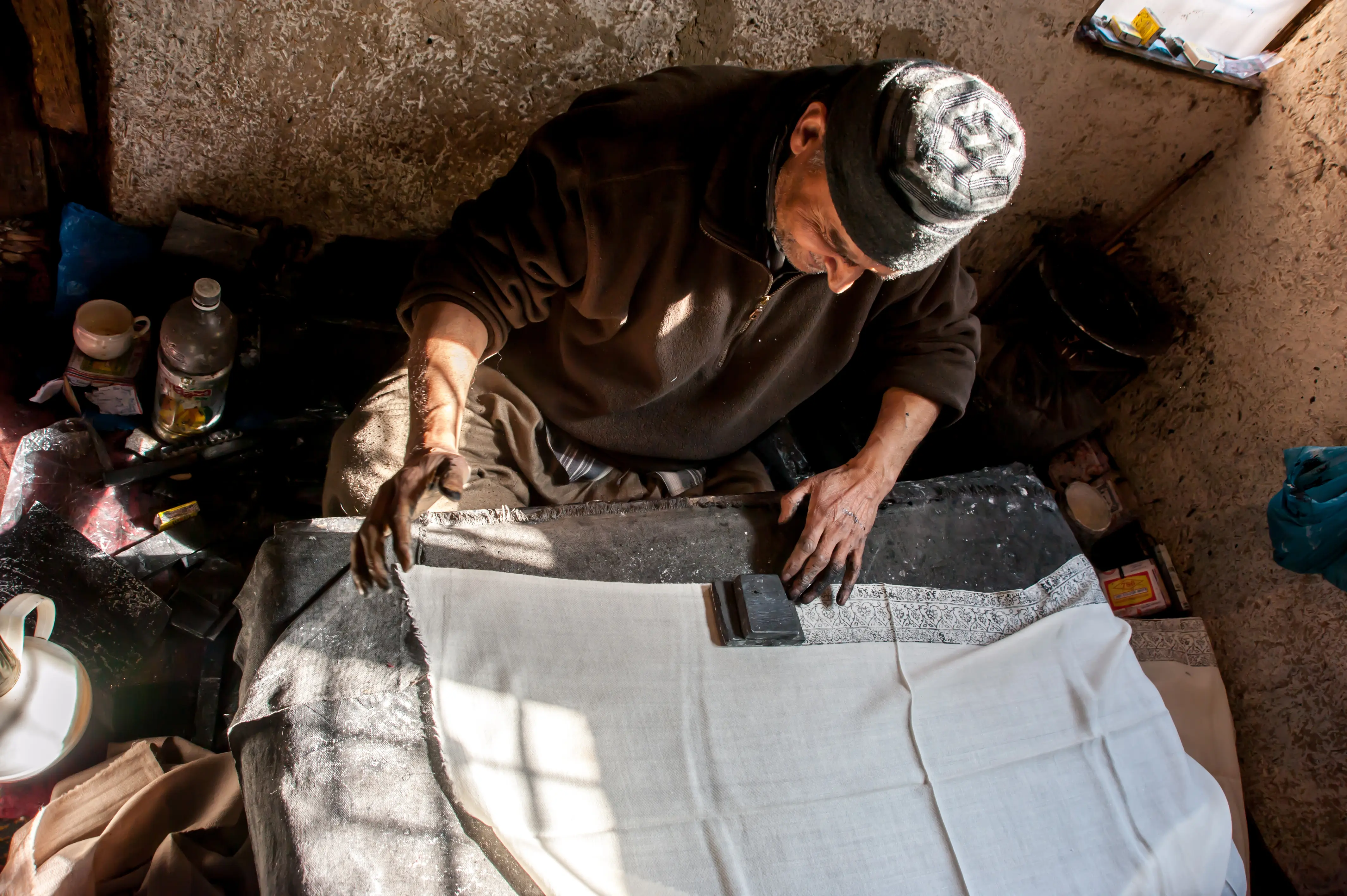 An artisan hand block-printing a pattern onto finished fabric