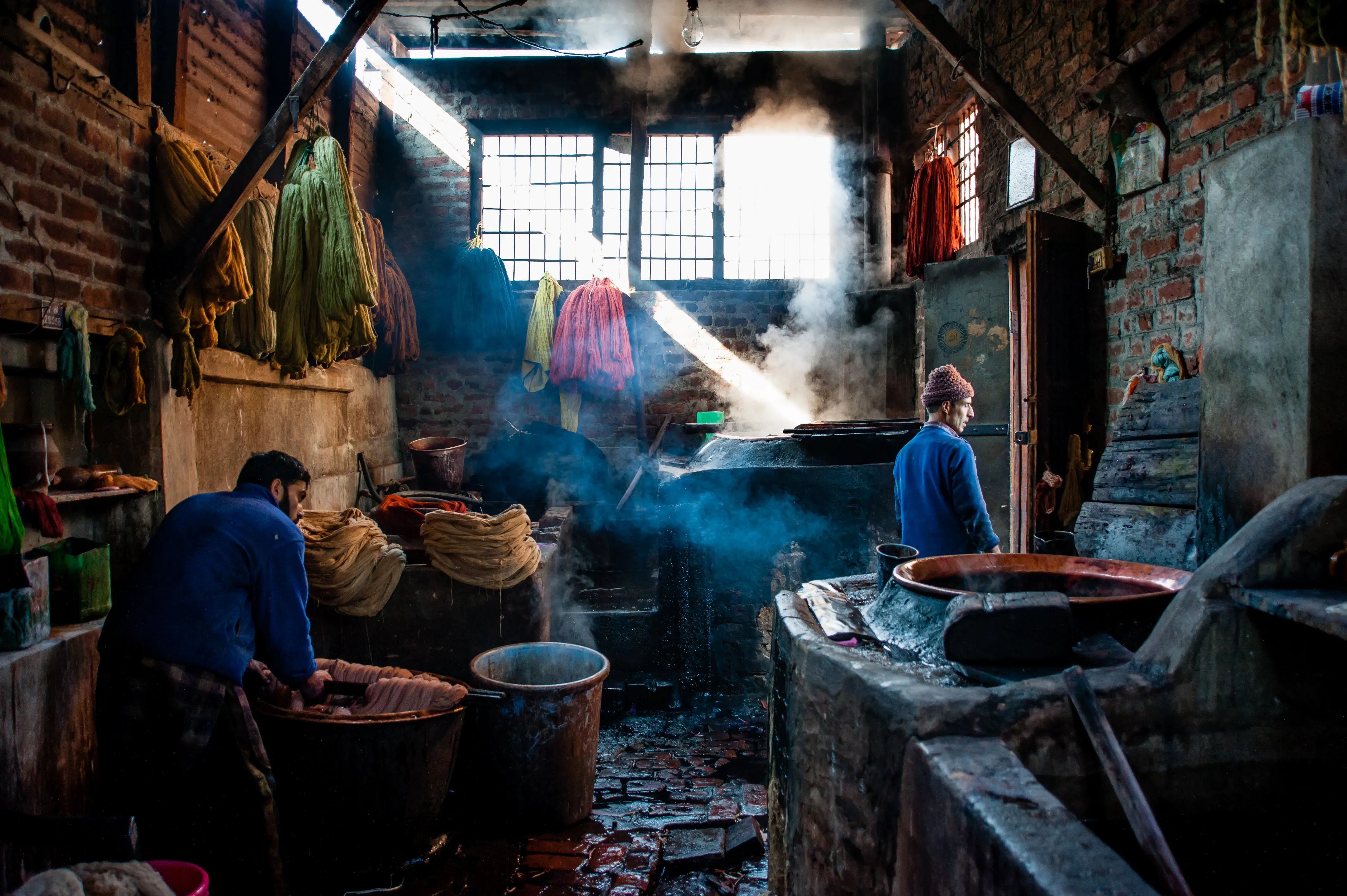 Artisans dyeing yarn in a workshop, steam rising and skeins of colour hanging to dry