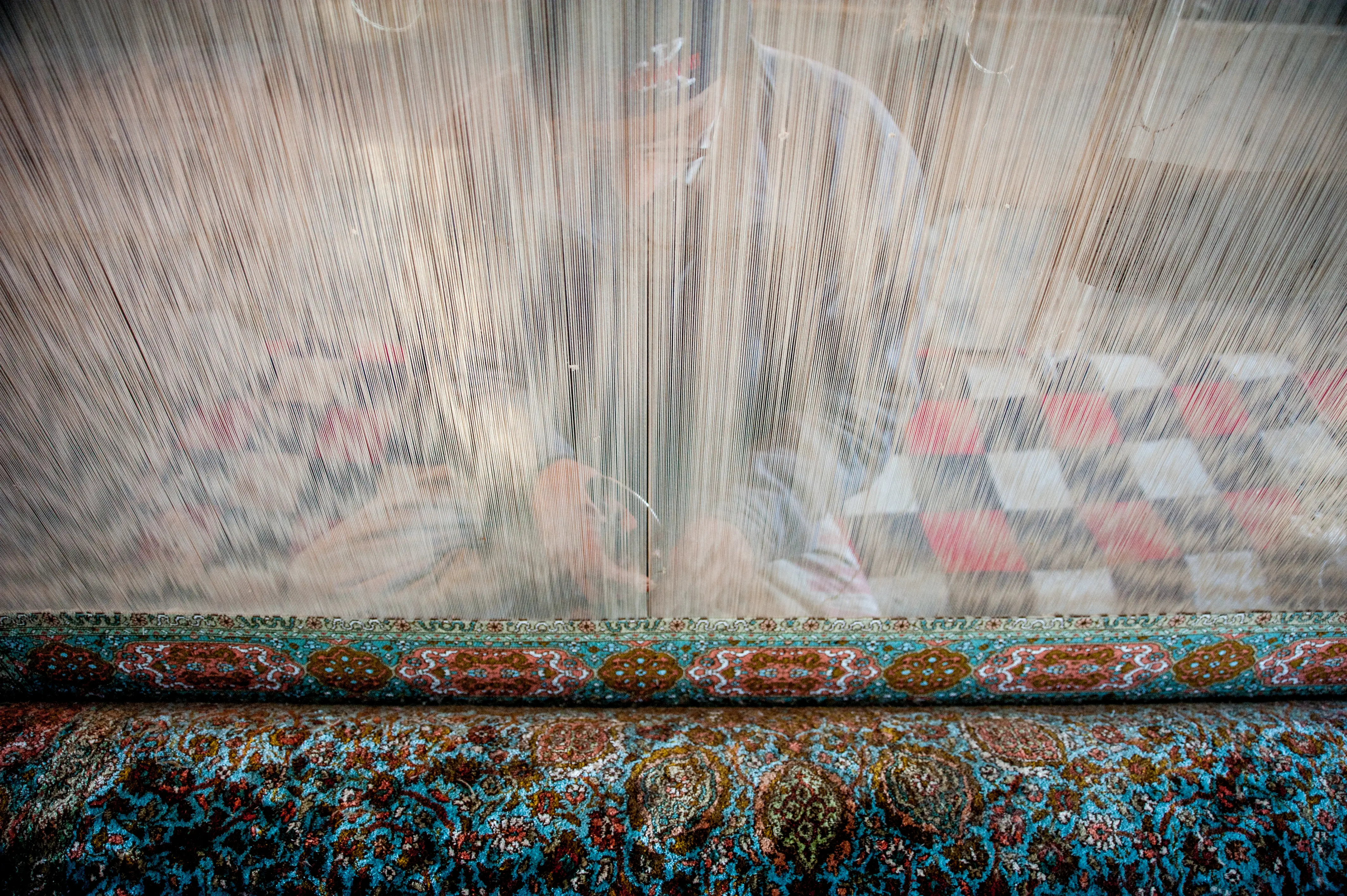 A finished hand-knotted carpet, seen through the warp threads of a loom