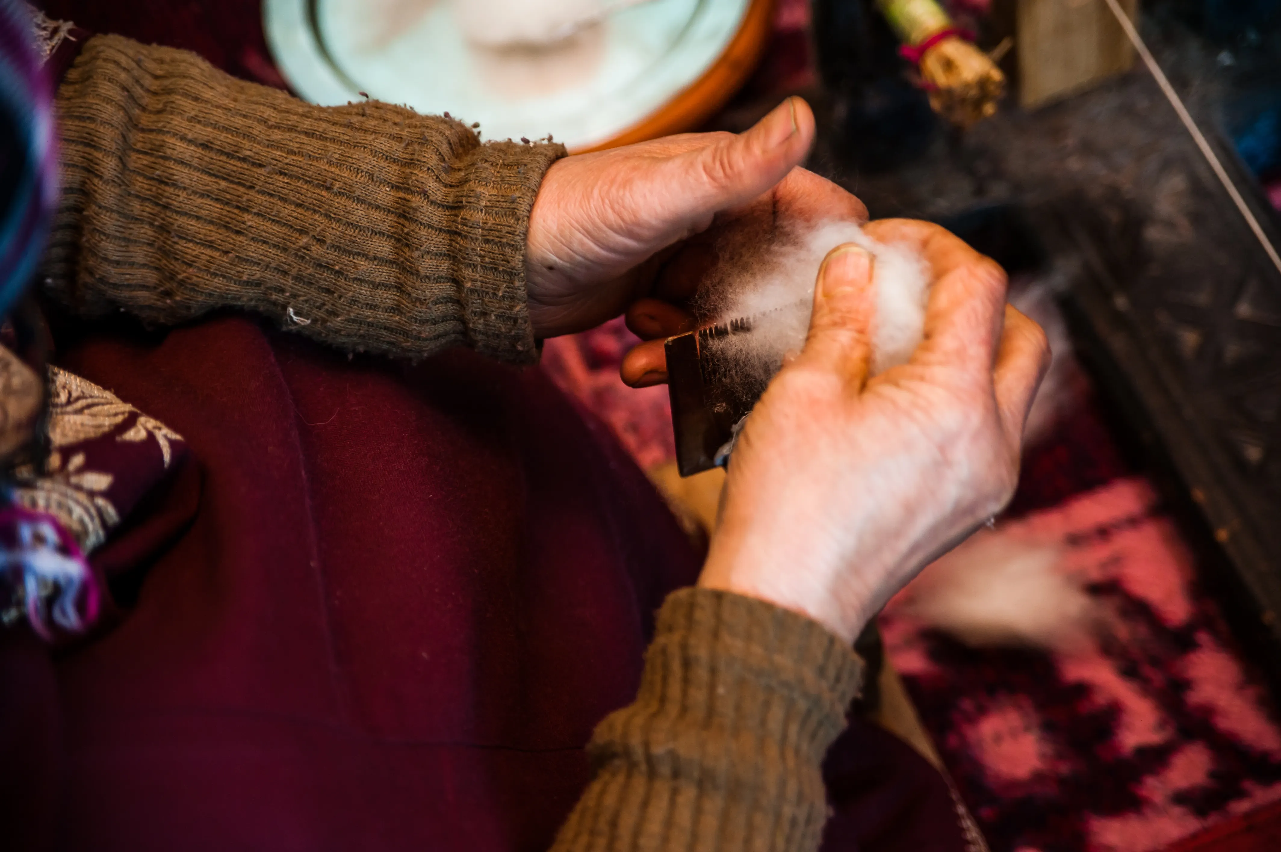 Hands carding raw pashmina fibre with a wooden card
