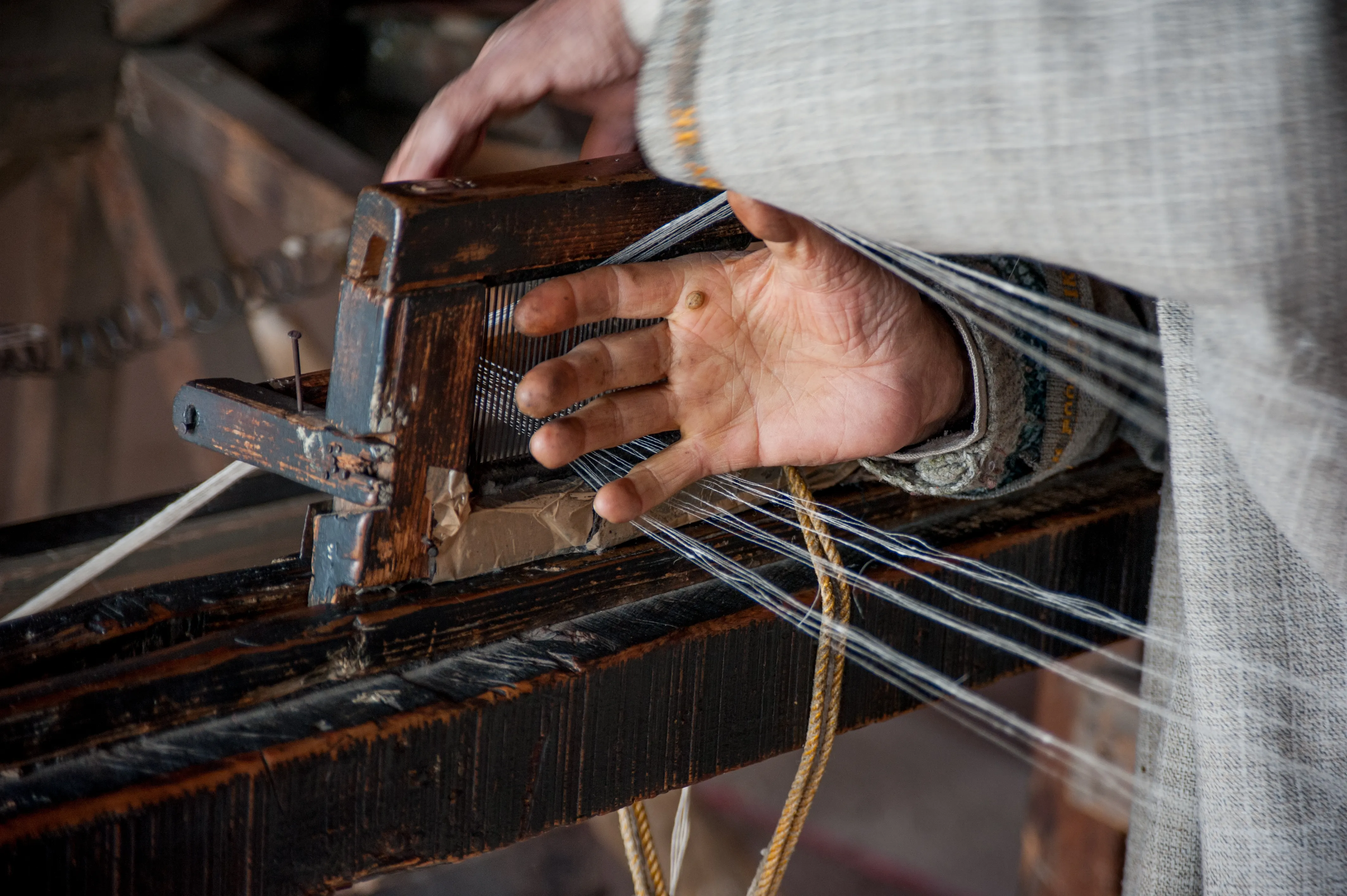 A weaver's hand guiding warp threads through a loom's reed
