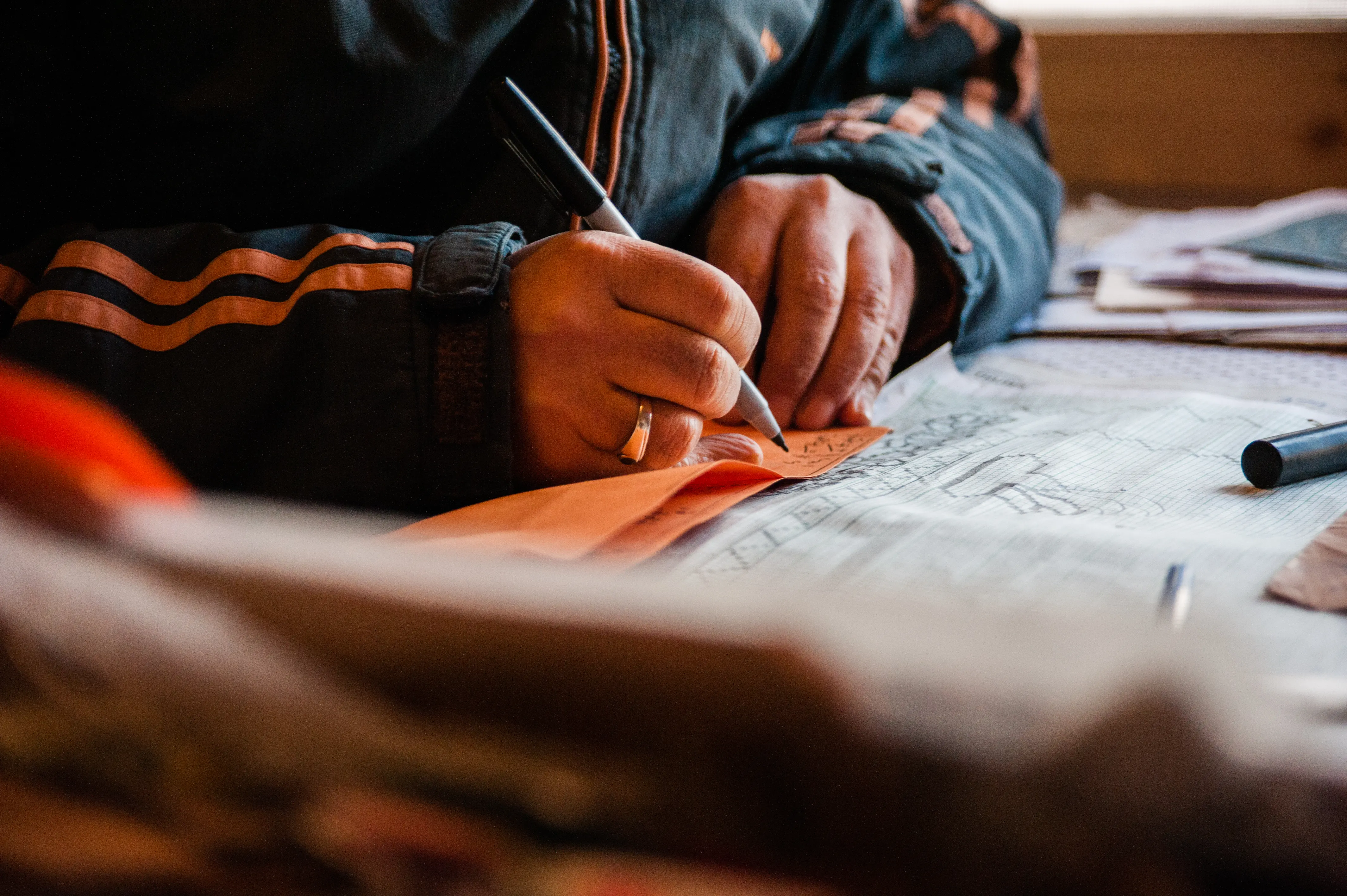 An artisan hand-marking a woven pattern chart, or talim, on graph paper