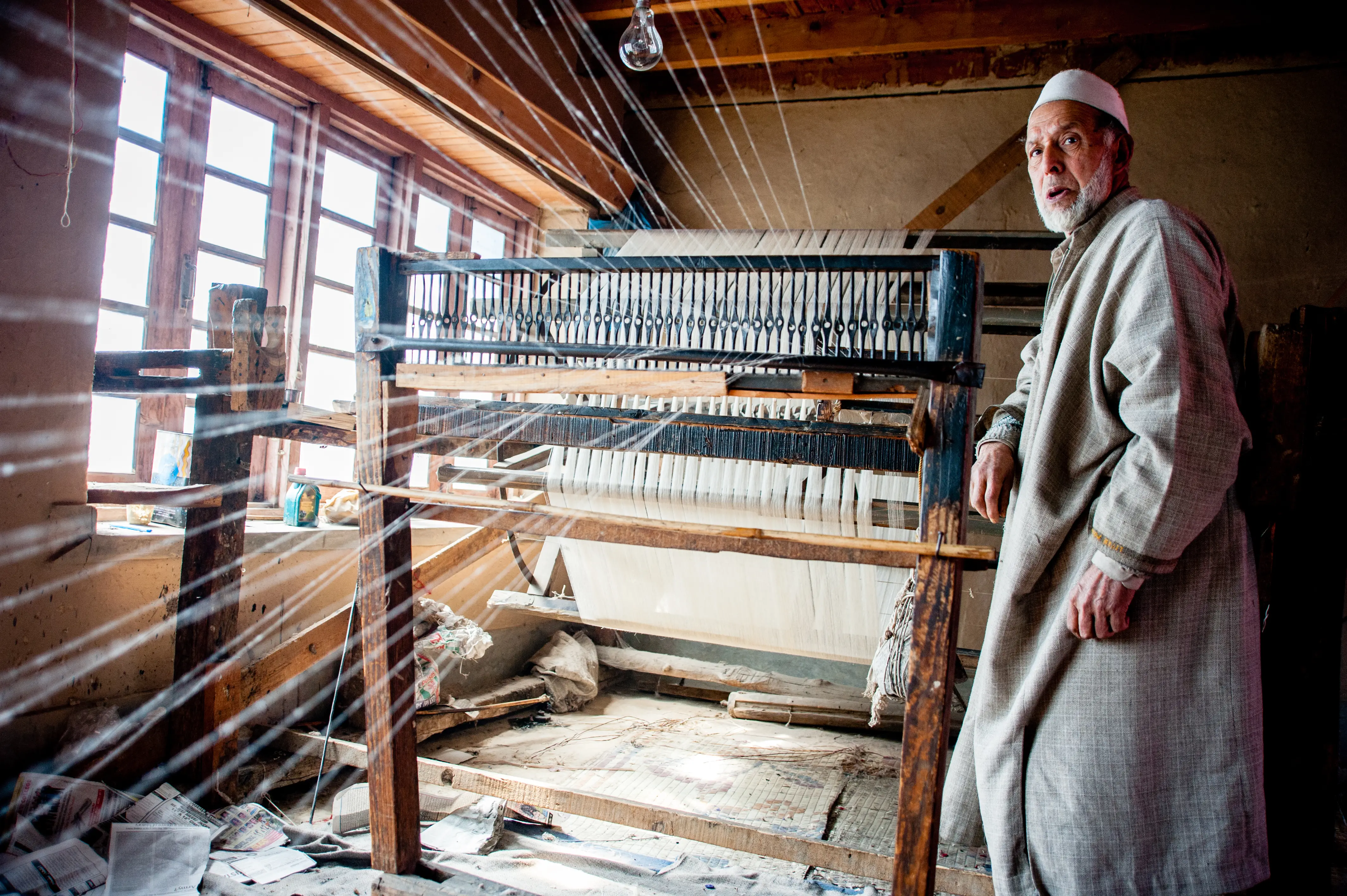 A weaver at a traditional handloom in Srinagar, seen through streaming warp threads